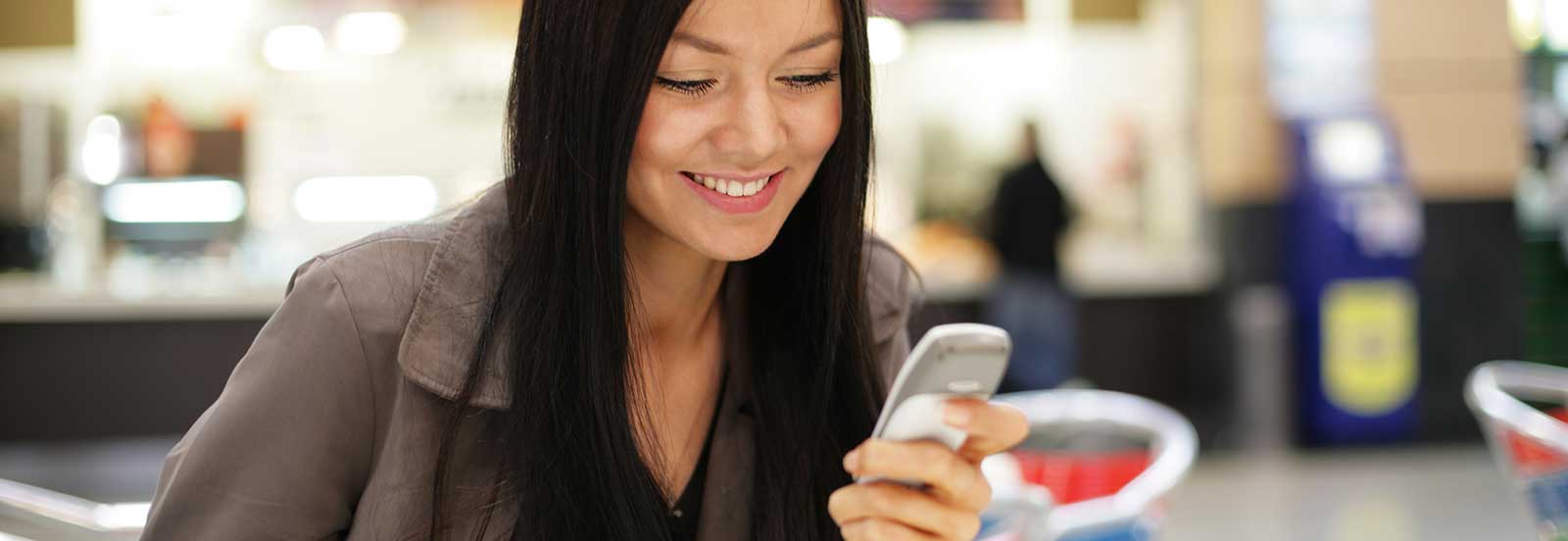Lady looking at a cell phone with a blurry background. - 1600x552