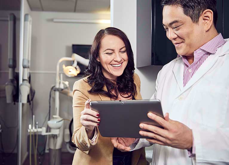 Male dentist showing a woman something on a tablet in a dentist office. - 767x554.jpg